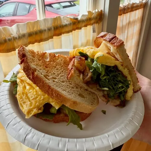 A breakfast sandwich on grilled sourdough with egg, bacon and greens