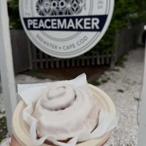 A frosted cinnamon roll held up in front of the Peacemaker window sign